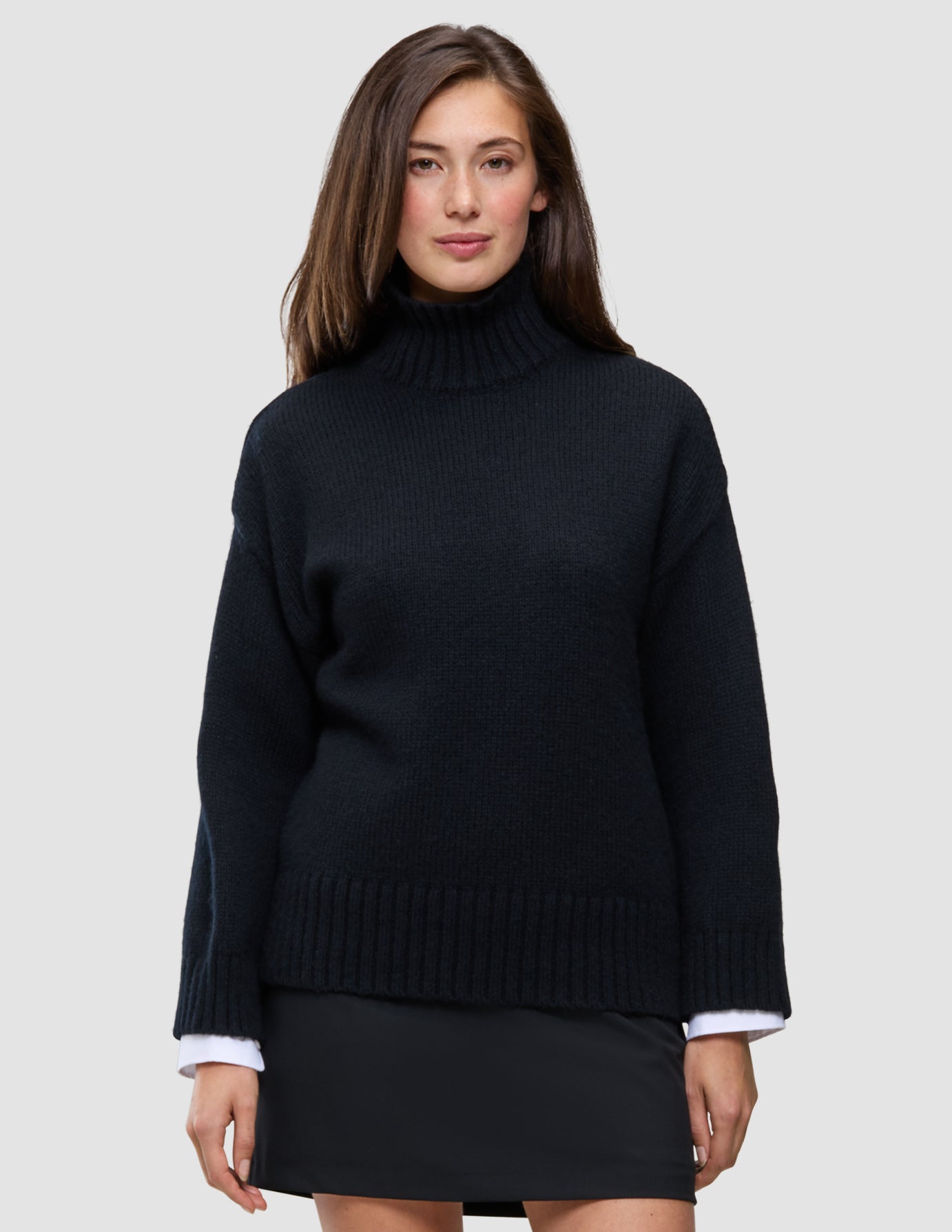 En person har på seg en svart, tykk og myk ullstrikket turtleneck for kvinner med vide ermer over en hvit skjorte.
